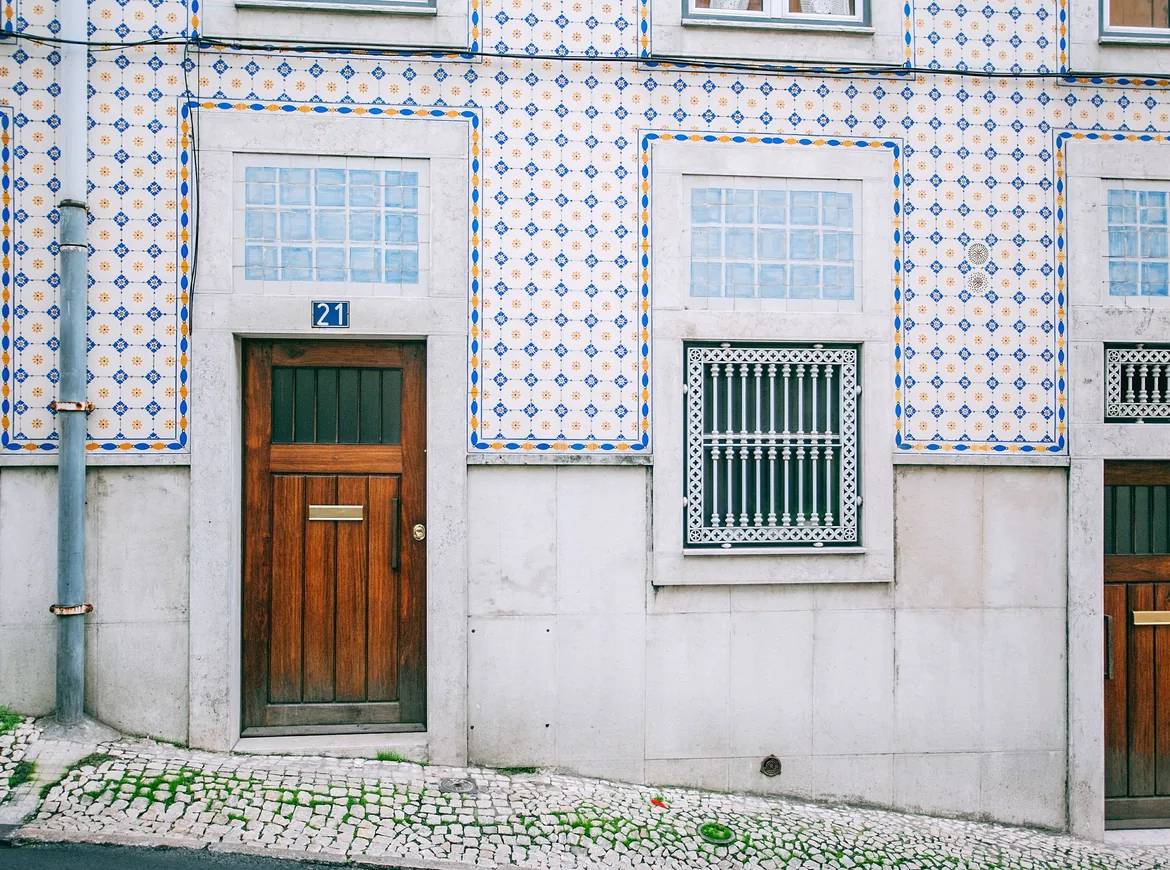 A white house front covered in blue-and-yellow tiles, with two wooden doors above a cobbled pavement