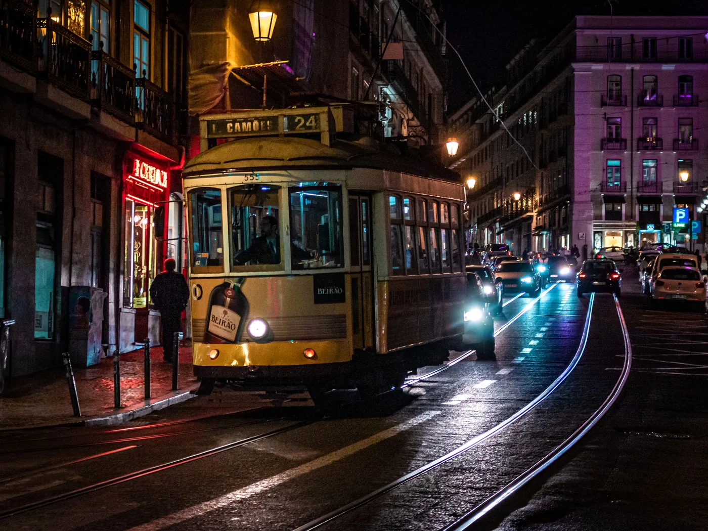 A yellow tram rounding a bend in a Lisbon street at night, its headlight shining on the rails